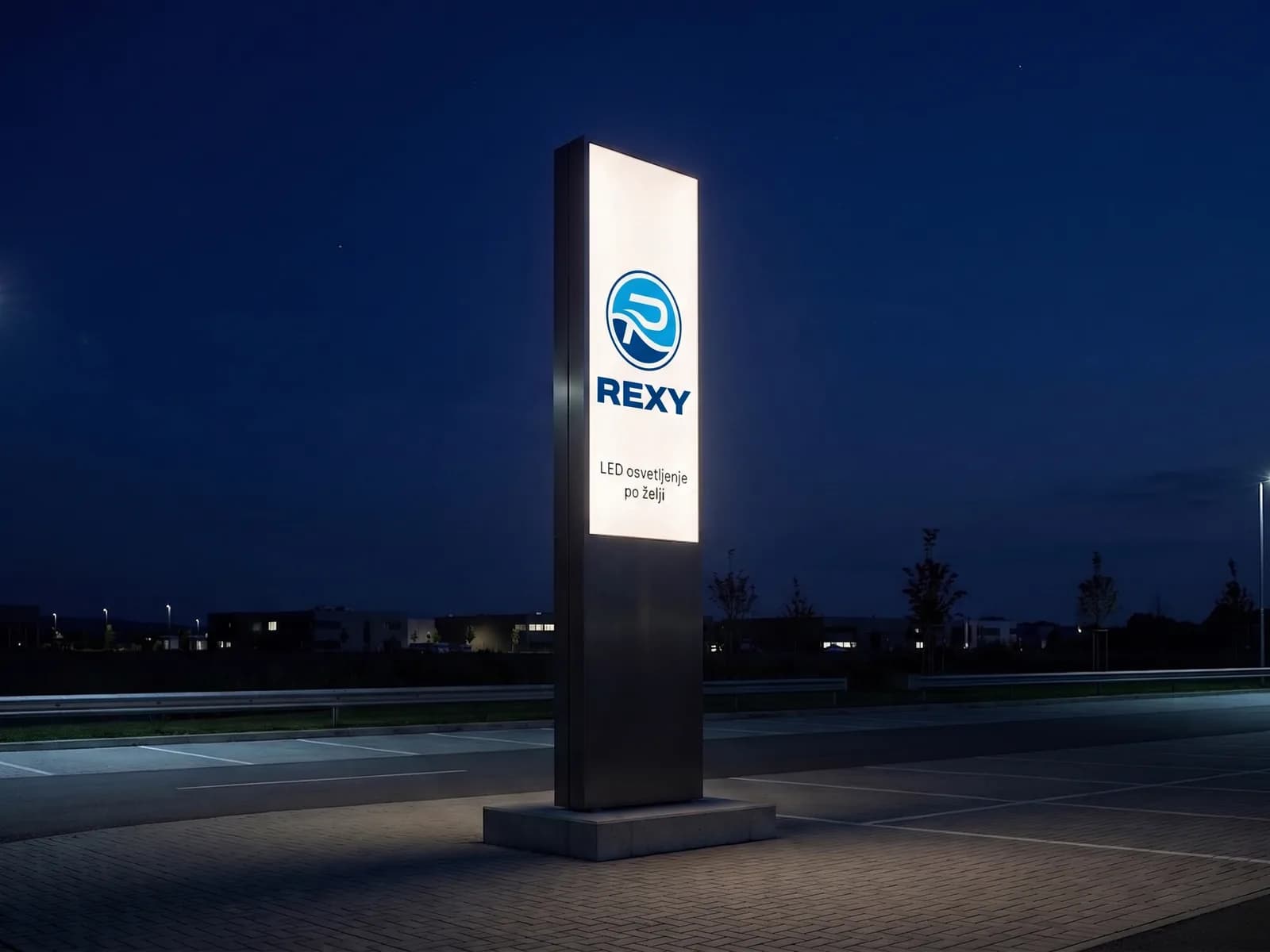 Isti totem noću — belo svetleće lice od klirita u tamnom aluminijumskom okviru, na parkingu poslovnog kompleksa
