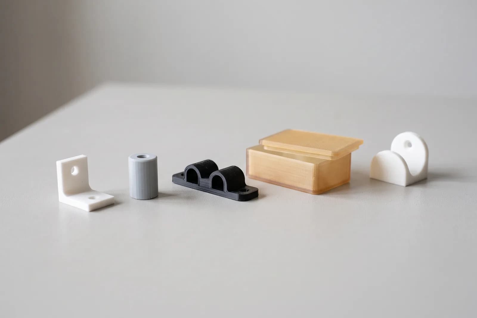 Delovi 3D štampani u PLA i PETG-u — ugaoni nosač, distancer, držač kabla, kućište i zidni nosač na radnom stolu