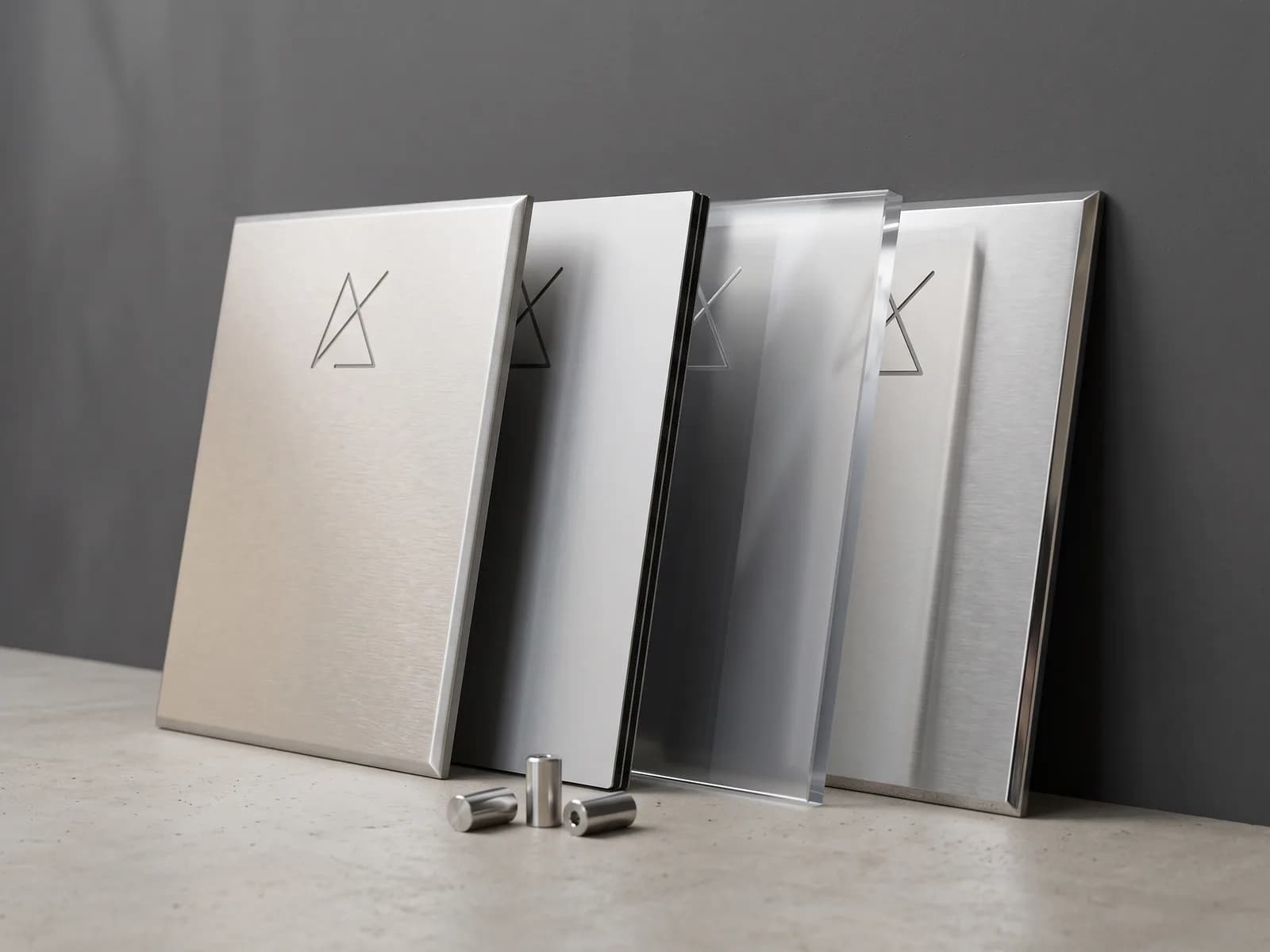 Četiri natpisne table u različitim materijalima naslonjene uz zid — aluminijum, alu bond, klirit i INOX, uz distancere